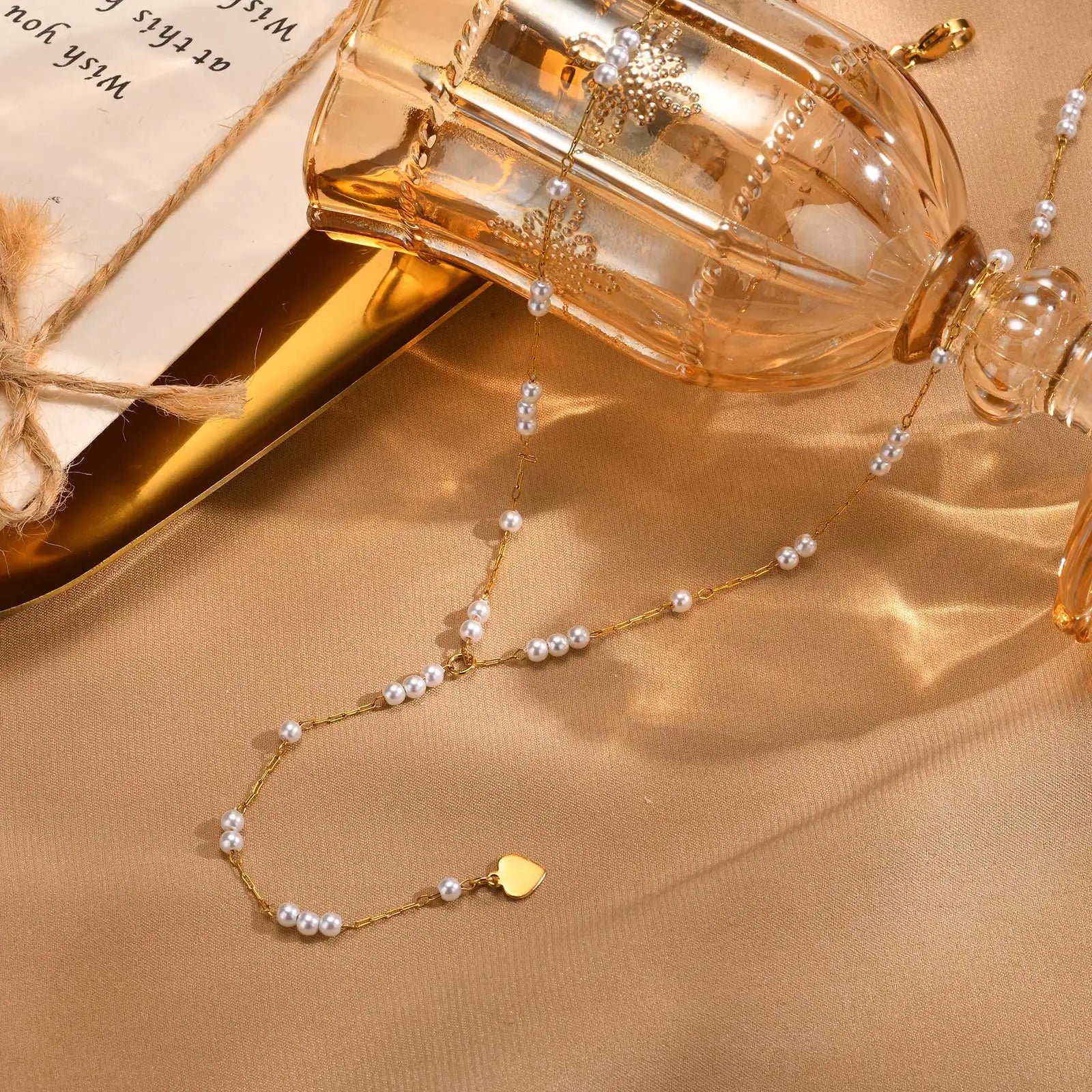 Elegant gold pearl heart pendant necklace displayed with a stylish bottle and soft fabric backdrop